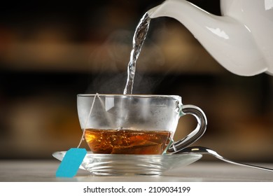 Pouring hot water into glass cup with tea bag on table against blurred background - Powered by Shutterstock