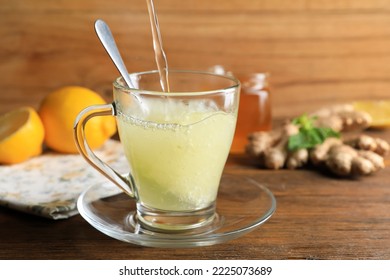 Pouring hot water into glass cup with grated ginger on wooden table