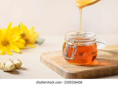 Pouring Jerusalem artichoke syrup in glass jar on biege background. Close up. Sugar substitute for healthy desserts. Natural sweetener.