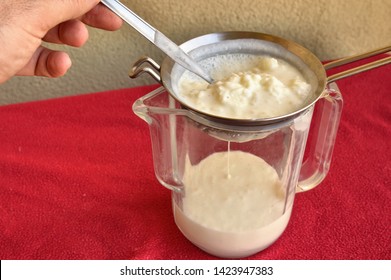 Pouring Of The Kefir, The Hand Of A Caucasian Man Gently Moves The Granules In The Sieve With A Spoon To Separate Them From The Fermented Milk.