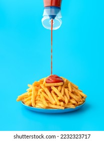 Pouring ketchup from a bottle over french fries, minimalist on a blue background. Delicious meal, french fries with ketchup in bright light on a colorful table. - Shutterstock ID 2232323717