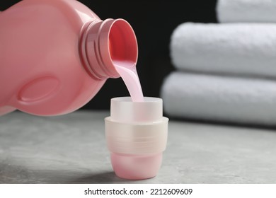 Pouring laundry detergent from bottle into cap on light grey marble table, closeup