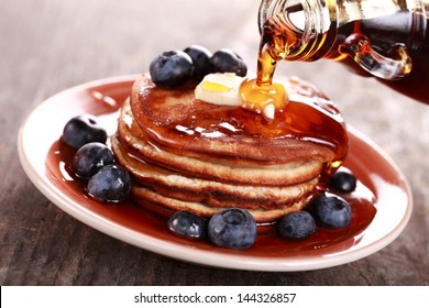 Pouring maple syrup on stack of pancakes