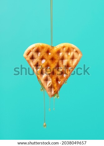 Pouring maple syrup over one heart-shaped waffle against a green-colored background. Close-up of maple syrup dripping on a waffle.