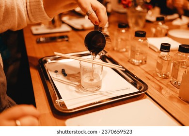 Pouring melted wax into glass. Set for crafting candle on metal tray. Master class of making candles. Beautiful female hands hold metal jug with wax. Creative occupation of making trendy diy candles.