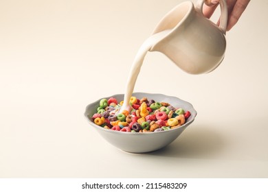 Pouring milk in bowl of colorful cereal rings on light background - Powered by Shutterstock