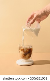 Pouring milk in coffee with ice cube on modern beige background. Vertical format. Iced latte coffee on modern still life. Vietnamese iced coffee. - Shutterstock ID 2006281001