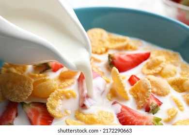 Pouring milk into bowl with crispy corn flakes and strawberries, closeup
