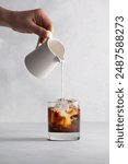 Pouring milk into coffee with ice in a glass.