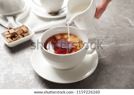Pouring milk into cup of black tea on table