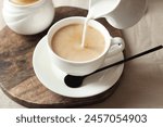 Pouring milk into cup with tea on light table, closeup