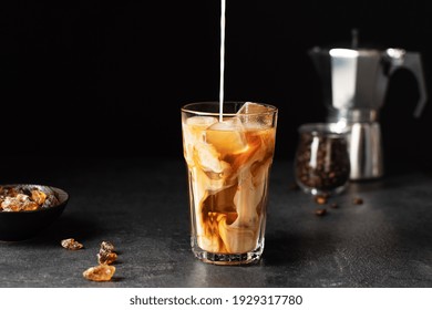 Pouring milk into a glass with iced coffee over black background. Cold refreshment summer drink. - Shutterstock ID 1929317780