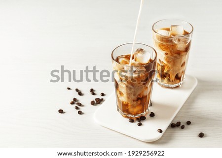 Pouring milk into glass with iced coffee. Cold refreshment summer drink.
