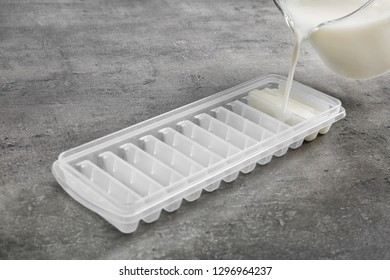 Pouring Milk Into Ice Cube Tray On Grey Table