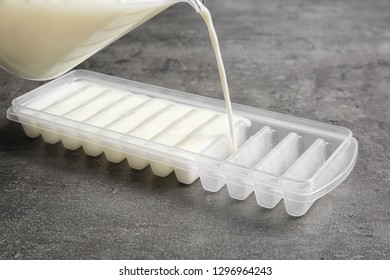 Pouring Milk Into Ice Cube Tray On Grey Table