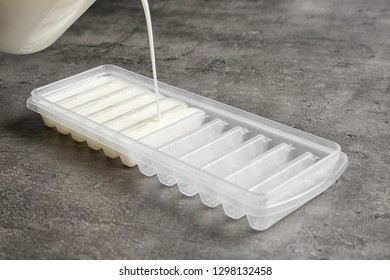 Pouring Milk Into Ice Cube Tray On Grey Table