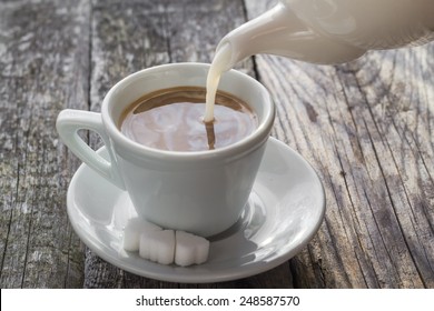 Pouring milk from a jug into a cup of black coffee