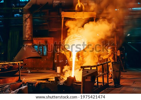 Pouring molten metal into mold from ladle container in foundry metallurgical factory workshop, iron cast, heavy industrial background