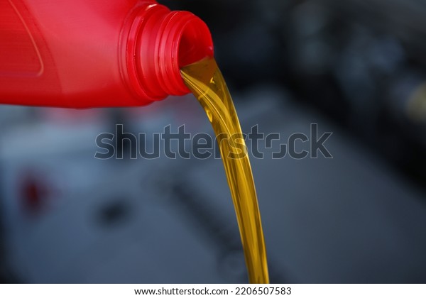 Pouring motor oil from red container against\
blurred background,\
closeup
