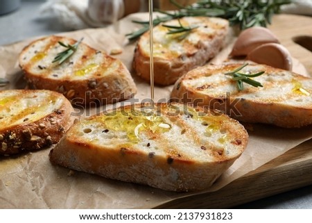 Pouring oil onto slice of toasted bread on wooden board, closeup