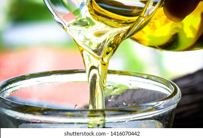 Pouring Olive Oil In The A Glass Bowl At Stone Kitchen And Inside Green Garden View. Prepare For Cooking Concept. Healthcare And Beauty Concept.