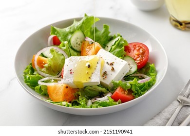 Pouring olive oil on greek salad with green leaves, tomatoes, cucumber, feta cheese. White bowl, marble background - Powered by Shutterstock