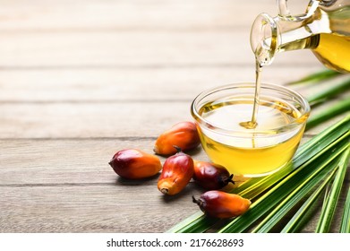 Pouring palm oil into glass bowl with fresh palm nuts on wooden table.