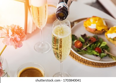 Pouring prosecco sparkling wine in a glass on sunday brunch with blurred eggs royal on the background.