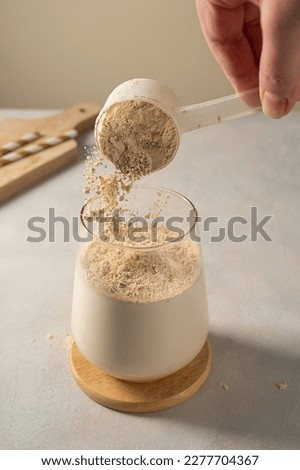 Pouring protein powder from scoop, in glass with milkshake. 