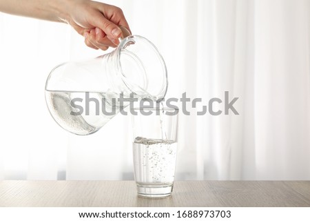 Pouring purified fresh water from the jug in glass on wooden table