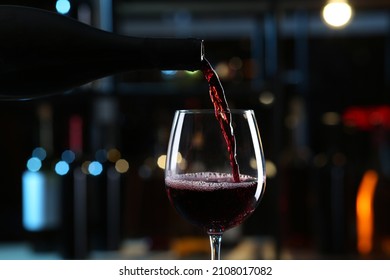 Pouring red wine from bottle into glass on blurred background, closeup - Shutterstock ID 2108017082