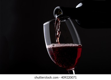 Pouring red wine from bottle into the wineglass on black