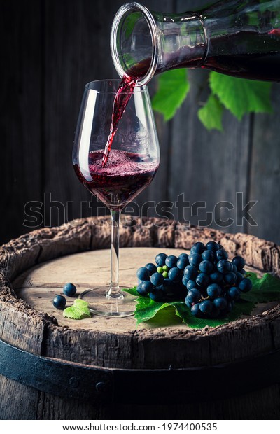 Pouring red wine from carafe into a glass and\
dark grapes. Wine\
industry.