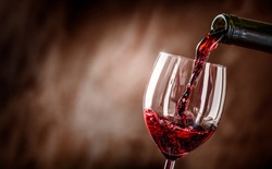 Pouring Red Wine Into The Glass Against Rustic Background.  Pour Alcohol, Winery Concept.