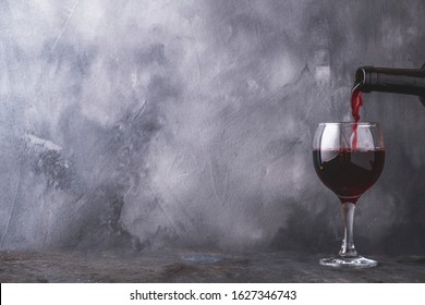 Pouring  red wine into glass on gray background. Copyspace
