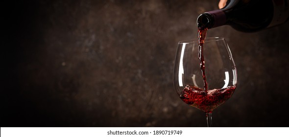 Pouring red wine into the glass against rustic dark wooden background - Powered by Shutterstock