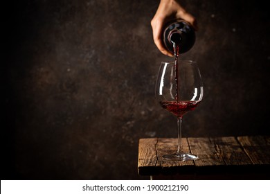 Pouring red wine into the glass against rustic dark wooden background - Shutterstock ID 1900212190