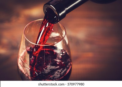 Pouring red wine into the glass against wooden background - Shutterstock ID 370977980