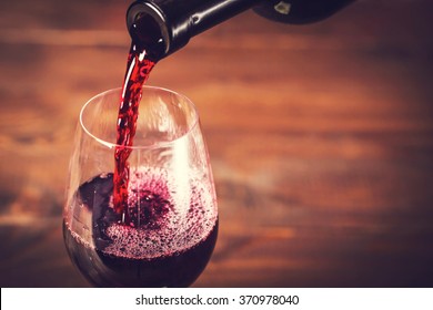 roter Wein in das Glas auf Holzhintergrund gießen