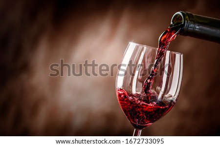 Pouring red wine into the glass against rustic background.  Pour alcohol, winery concept.