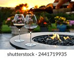 Pouring red wine into glasses at sunset golden hour next to a firepit fire table.
