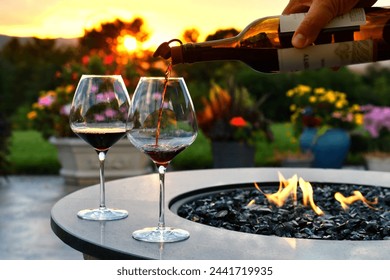 Pouring red wine into glasses at sunset golden hour next to a firepit fire table. - Powered by Shutterstock