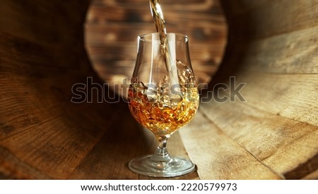 Pouring rum into glass inside old wooden barrel. Concept of fresh beverages.