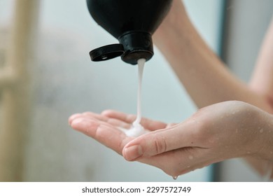 Vaciando champú de la botella con la mano femenina en el baño. Concepto de higiene