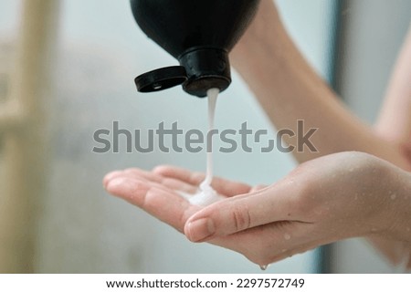 Pouring shampoo from bottle on female hand in bathroom. Hygiene concept