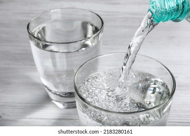 Pouring soda water from bottle into glass on white wooden table, closeup