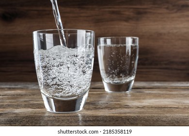 Pouring Soda Water Into Glass On Wooden Table. Space For Text