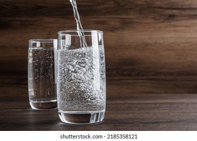 Pouring Soda Water Into Glass On Wooden Table. Space For Text