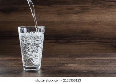 Pouring Soda Water Into Glass On Wooden Table. Space For Text