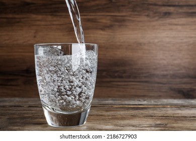 Pouring Soda Water Into Glass On Wooden Table. Space For Text